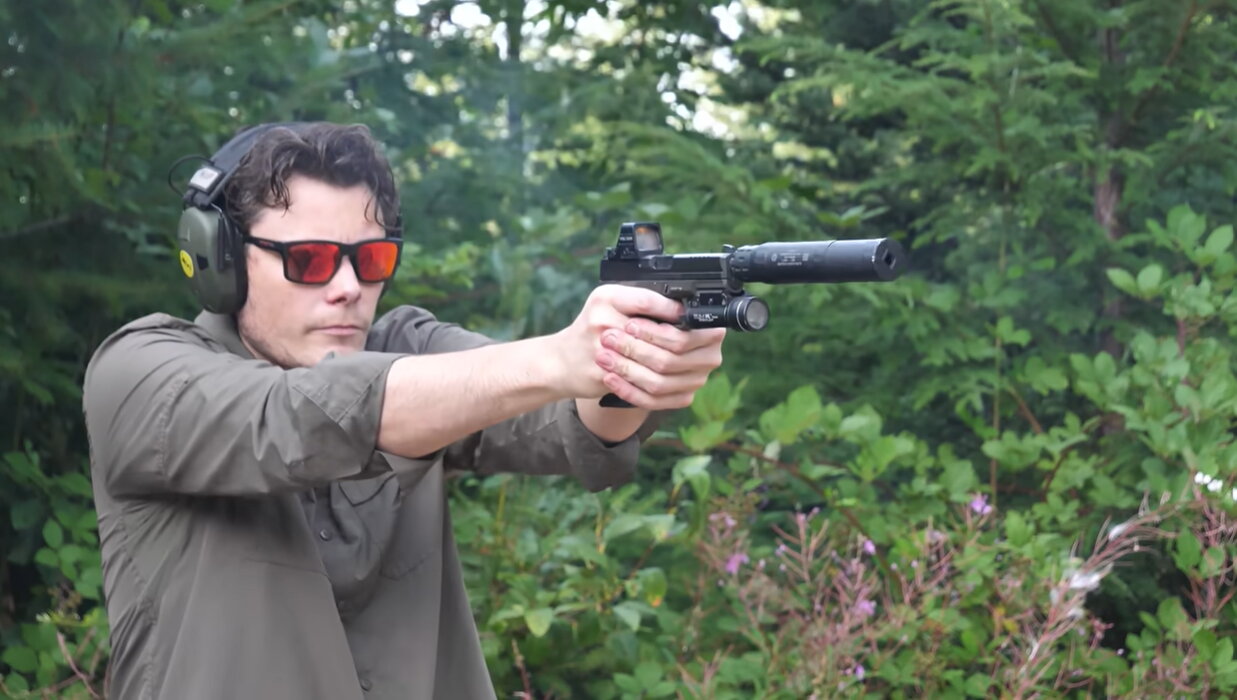 Shooter firing suppressed 9mm pistol outdoors