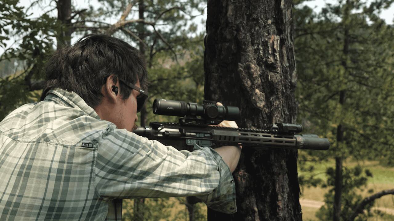 Shooter aims scoped 5.56 rifle outdoors