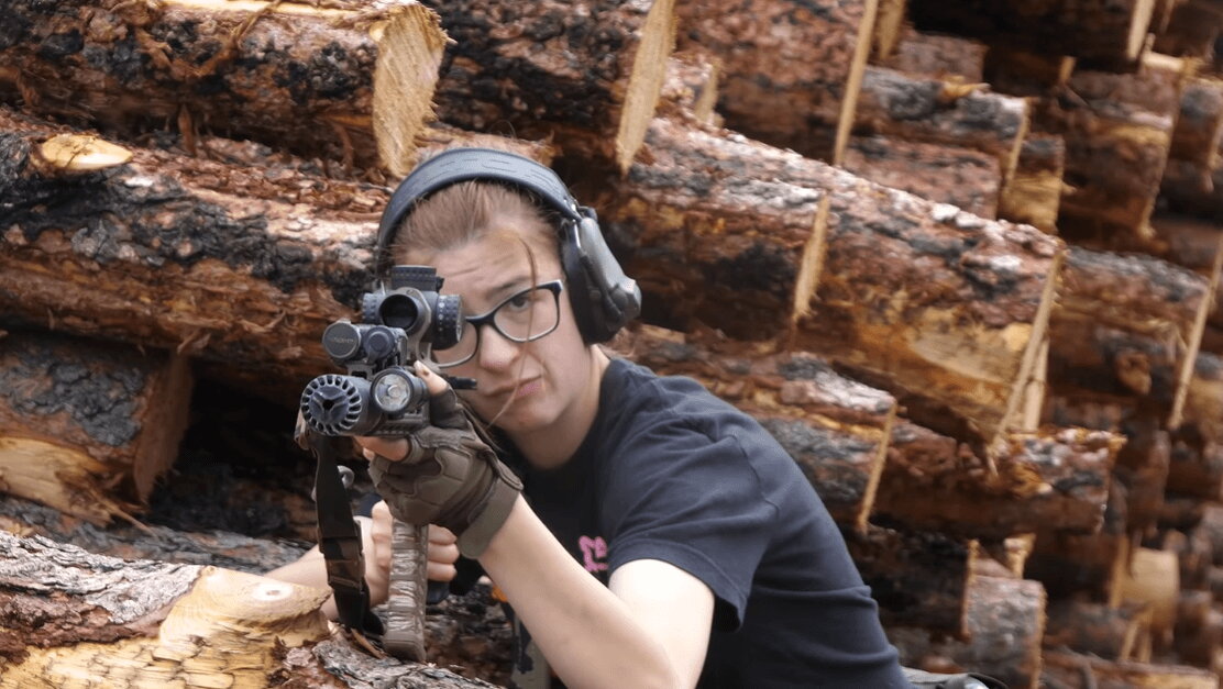 AR carbine shooter aiming behind logs